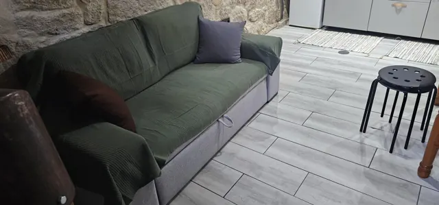 O sofá, encostado à parede de pedra.